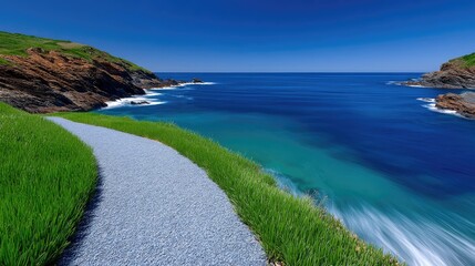 Coastal Path Meanders Beside Sparkling Blue Ocean Under a Clear Sky with Lush Green Grass and Rocky Outcroppings
