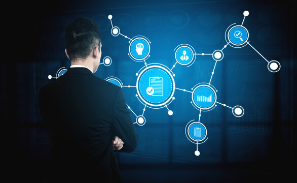 A businessman analyzes a digital network in a modern office setting, focusing on technology connections and data graphics that represent information management and growth. Tessel - Powered by Adobe