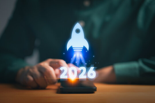 Person using a smartphone with a glowing rocket icon and 2026, symbolizing vision, future target planning, ambition, new ideas, innovation trends, digital strategy, and goal forecasting.