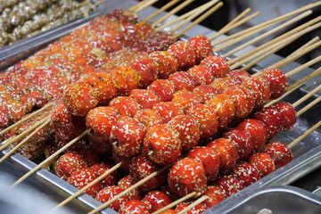 Close-up of various traditional Chinese tanghulu (sugar-coated fruit skewers) on display at a street food market.