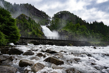 Powerful waterfall flowing under historic stone arch bridge