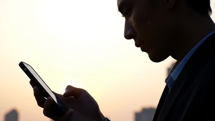 Silhouette of a young man using a smartphone outdoors at sunset with a soft warm glow in the background highlighting modern communication and digital connection. - Powered by Adobe