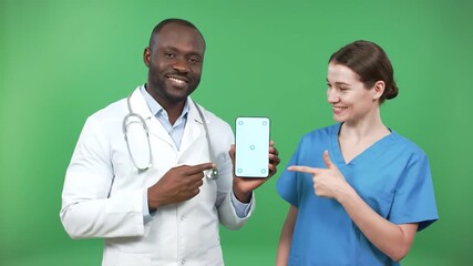 Two diverse medical professionals a male African American doctor and a female Caucasian nurse smiling and pointing at a smartphone with a green screen promoting healthcare technology and digital solu. - Powered by Adobe