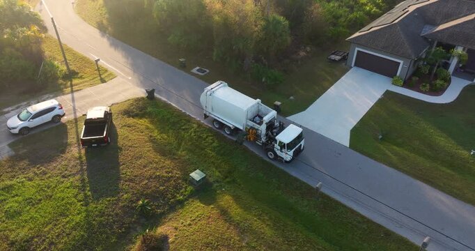 Garbage removal in residential area. Waste truck loading household rubbish while driving on suburban street.