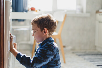 A young boy is focused on drawing on the refrigerator with a marker in a bright and inviting kitchen