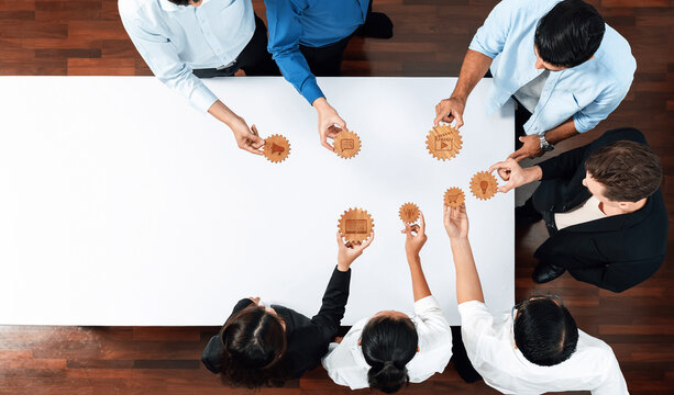 Aerial view of a diverse team of business professionals engaging in a collaborative strategy session with gears on a table, symbolizing teamwork and innovation in the workplace. Amity