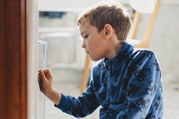A young boy is focused on drawing on the refrigerator with a marker in a bright and inviting kitchen