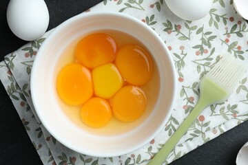 Raw eggs, yolks and brush on black table, flat lay