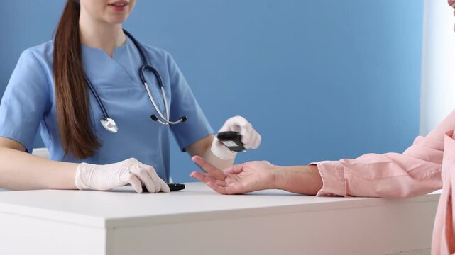 Diabetes. Smiling doctor in medical gloves checking patient's blood sugar level with lancet pen and glucometer at table in hospital. Camera moving forward