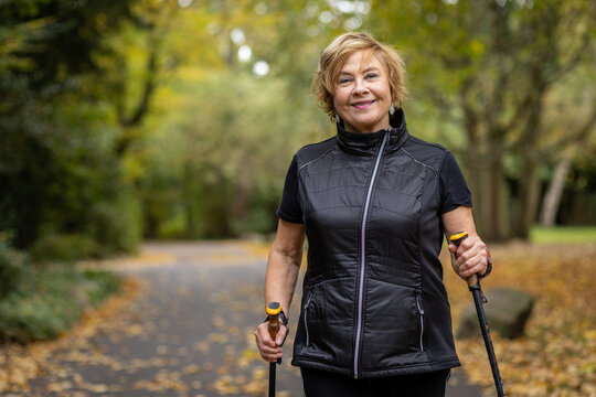 Senior woman enjoying a walk with Nordic poles in a colorful autumn park surrounded by falling leaves