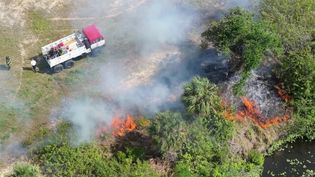 Scorching flames devour Florida forest vegetation during drought season, as firefighting crews arrive to contain widespread fire damage and thick smoke.