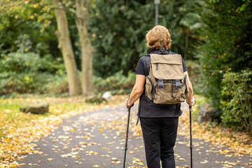 Hiking on a quiet path in autumn with a backpack and trekking poles near lush trees