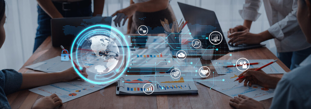 A dynamic business meeting with professionals collaborating around laptops and tables, featuring digital data visualization tools and global analytics for strategy development. Trope