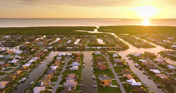 Sunset aerial view of Punta Gorda wealthy neighborhood. Expensive residential homes along canals reflect warm evening sky.