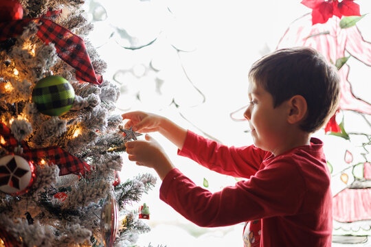 Young boy happily decorating a christmas tree by a window