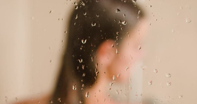 Girl enjoying a refreshing shower with water droplets glistening on the glass in a stylish bathroom setting during quiet morning hours