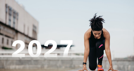An athlete is positioned at the starting line, focused and prepared for a race. The backdrop features urban architecture suggesting a modern city setting. The year 2027 is prominently displayed.