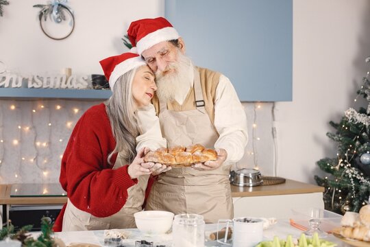 Senior couple in aprons and christmas red hats baking bread in kitchen