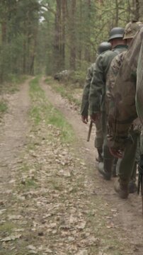 Group Of Reenactors Dressed As German Infantry Soldiers Marching By Forest Road Autumn Season. Reenactment Tactic Game. Carabin Mauser 98k. Wermacht German Military Uniform And Rifles During Ww2