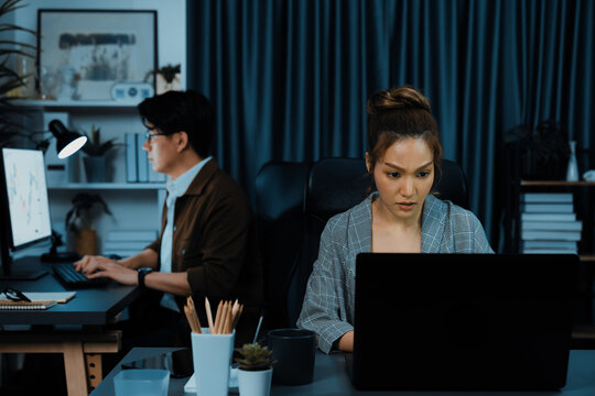 Serious face of thinking businesswoman focusing computer to report data analysis social media online project job with coworker working at back side at over late night time at modern office. Infobahn.