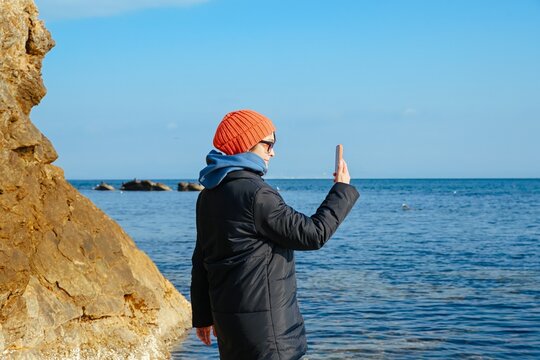 Mature Russian woman taking selfie by the Japan Sea in Vladivostok. Stylish traveler sharing her cold season journey on social media.
