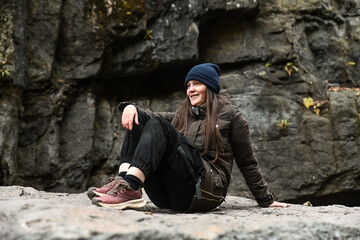 Russian woman traveler sitting on a rock near a waterfall. Autumn hike adventure in the mountains, enjoying nature and outdoor freedom.