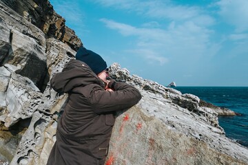 Russian woman tourist in warm clothes enjoys the winter sea view from rocky cliffs on the coast of the Japanese Sea in Vladivostok, Russia.