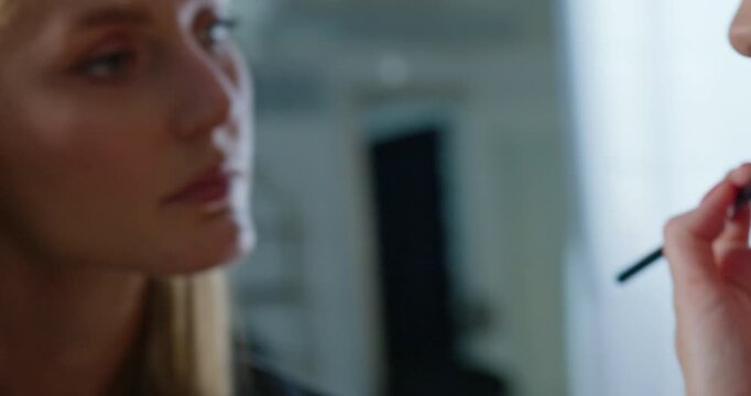 Close up of a makeup artist applying nude lipstick to a model lips in slow motion