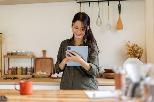 Asian woman using digital tablet in a kitchen using laptop at home, Activity lifestyles concept

