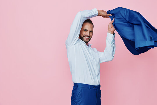 An executive man in a crisp shirt cheerfully removes a blue jacket, standing against a soft pink backdrop. He exudes confidence, focus, and professional pride in a dynamic moment.