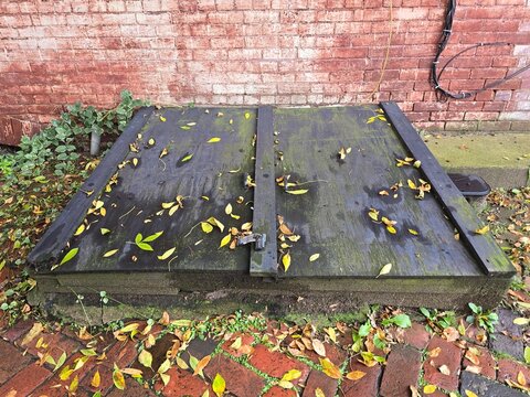 Antique Cellar door in a sidewalk against a red brick wall