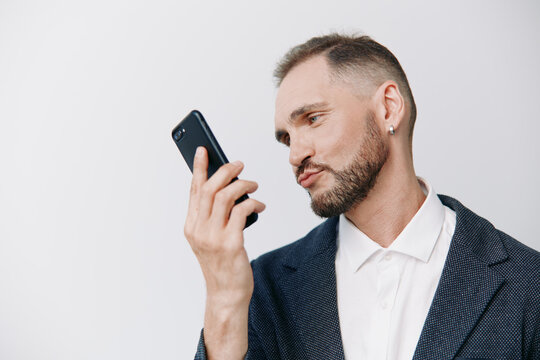 A business professional man stands with a focused expression, using a mobile device against a solid colored background, conveying calm confidence and executive presence.