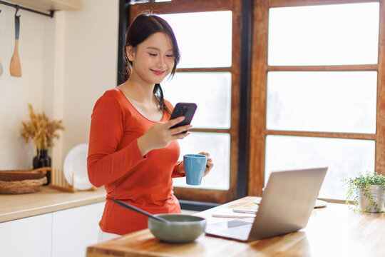 Happy asian woman drinking tea while using smart phone in the kitchen. Copy space.
- Powered by Adobe