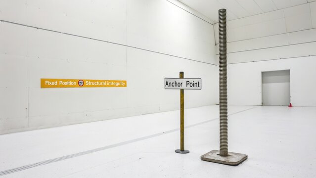 A sturdy metal anchor point sign stands in a minimalist white space next to a tall ribbed metal column