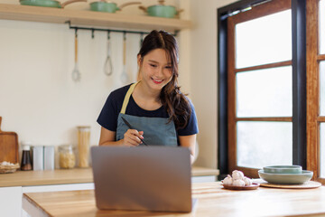 Woman, cooking in kitchen with laptop for live streaming, online recipe and meal prep by stove. Nutrition influencer, food blogger or vegan chef with social media tutorial in apartment
