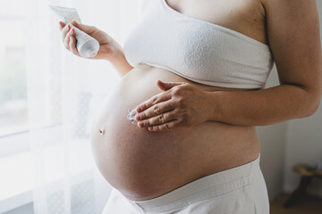 A pregnant woman applies skincare cream to her skin. This moment emphasizes self-care during pregnancy.