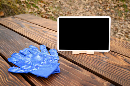 a blue gardening glove and a white tablet on a stand are on a brown wooden table