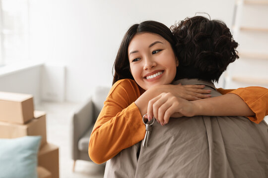 Young couple happily celebrates moving into their new home. The woman joyfully hugs her boyfriend, holding a house key, filled with excitement on this special day.