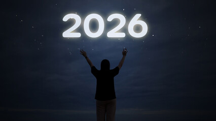 Person with arms raised celebrating the New Year 2026, watching colorful fireworks light up the night sky for the holiday countdown.