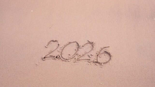 Hand writing the year 2026 in the sand, concept for business planning, new year's goals, work-life balance, or financial freedom.