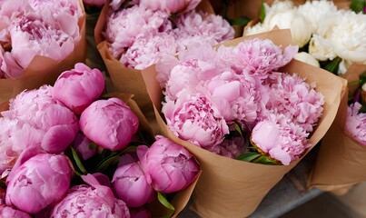 several bouquets of fresh pink peonies wrapped in brown paper, arranged closely together on a market stall