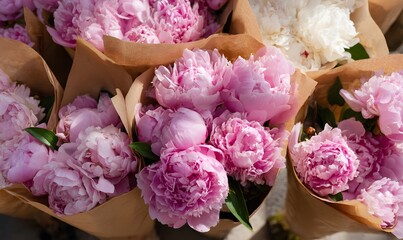 several bouquets of fresh pink peonies wrapped in brown paper, arranged closely together on a market stall
