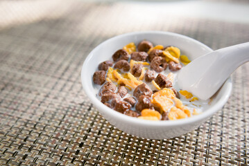 A bowl of mixed corn flakes and chocolate cereal served with milk and a spoon, a delicious and popular breakfast choice that combines crunchiness and sweetness in every bite.