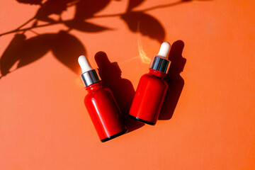 Red Glass Serum Bottles with Dropper on Bright Orange Background Skincare Concept