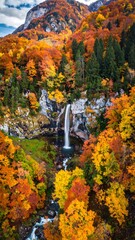 Cascading waterfall surrounded by vibrant autumn foliage with mountain backdrop