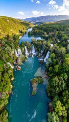 Cascading waterfall tumbles into a turquoise river amidst lush, green, rolling hills