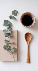 Minimalist still life featuring eucalyptus, a cup of coffee, a wooden spoon, and a book