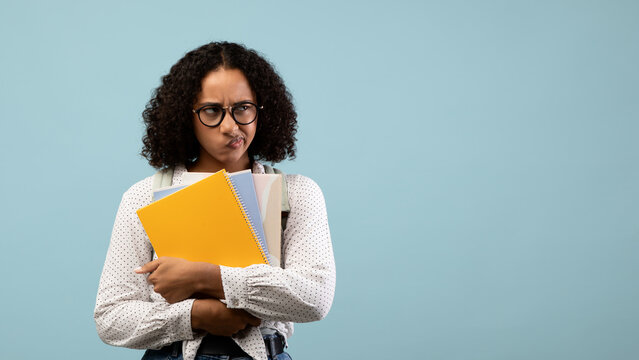 A black female student stands with a backpack and notebooks, showing frustration and stress as she gazes into empty space. The blue background emphasizes her feelings of pressure related to education.