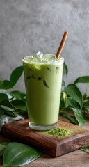 Iced matcha latte in glass with ice, wooden stand, and green leaves