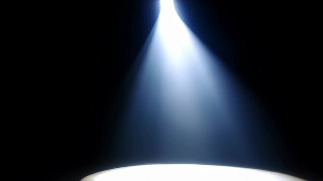 Single bright white spotlight beam illuminates dark empty stage with diffused light rays in a dramatic atmospheric performance setting